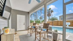 A covered patio with a pool, wooden chairs, and a door. - Beach Happy 315–Step-Free 3BR Near Beach–Pool+Cart (Panama City Beach)