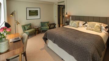 A hotel room with a large bed, a desk with a laptop, a chair, and a small table with a vase of flowers.