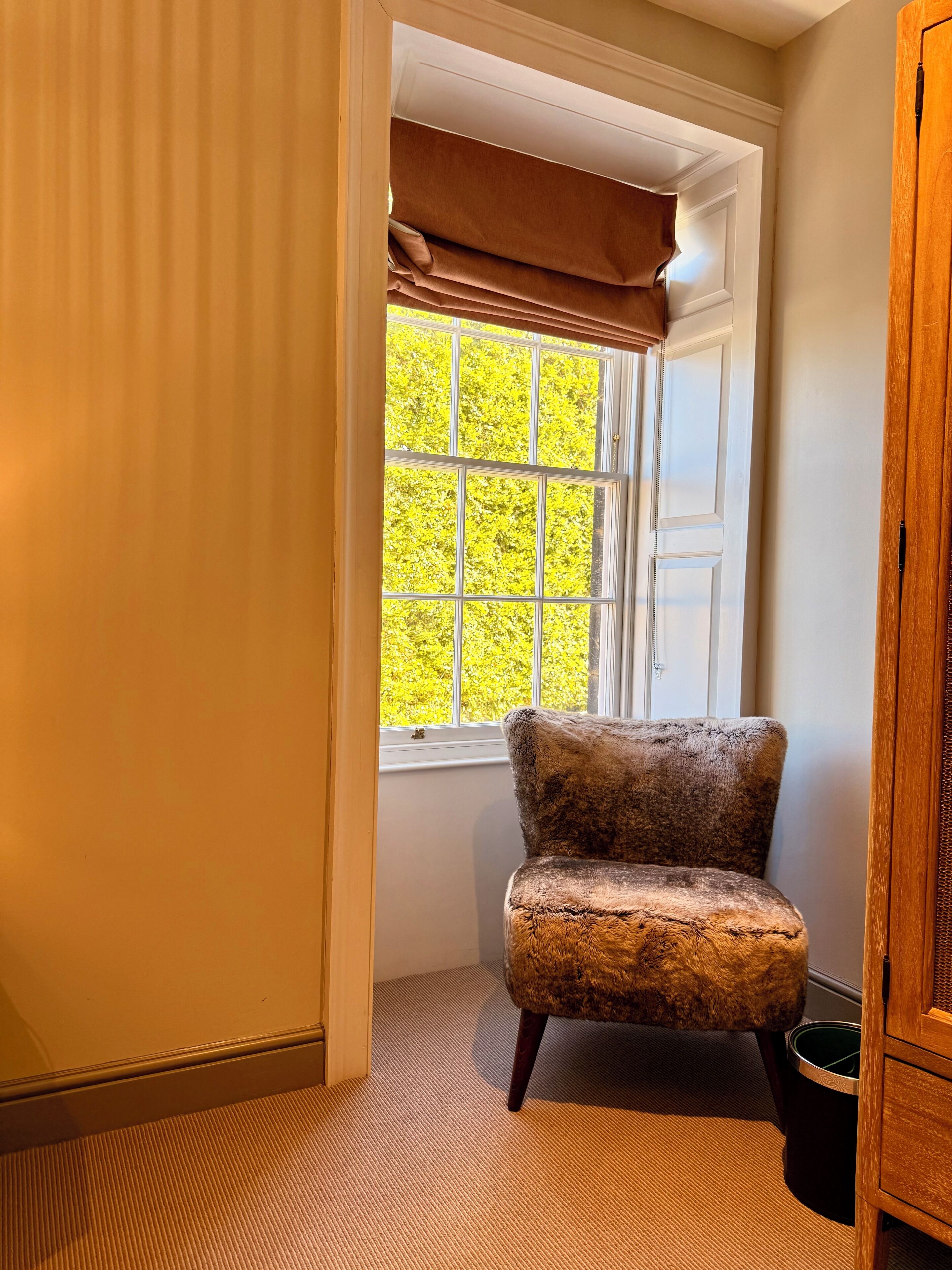 A corner room with a window, a chair, and a wooden cabinet.