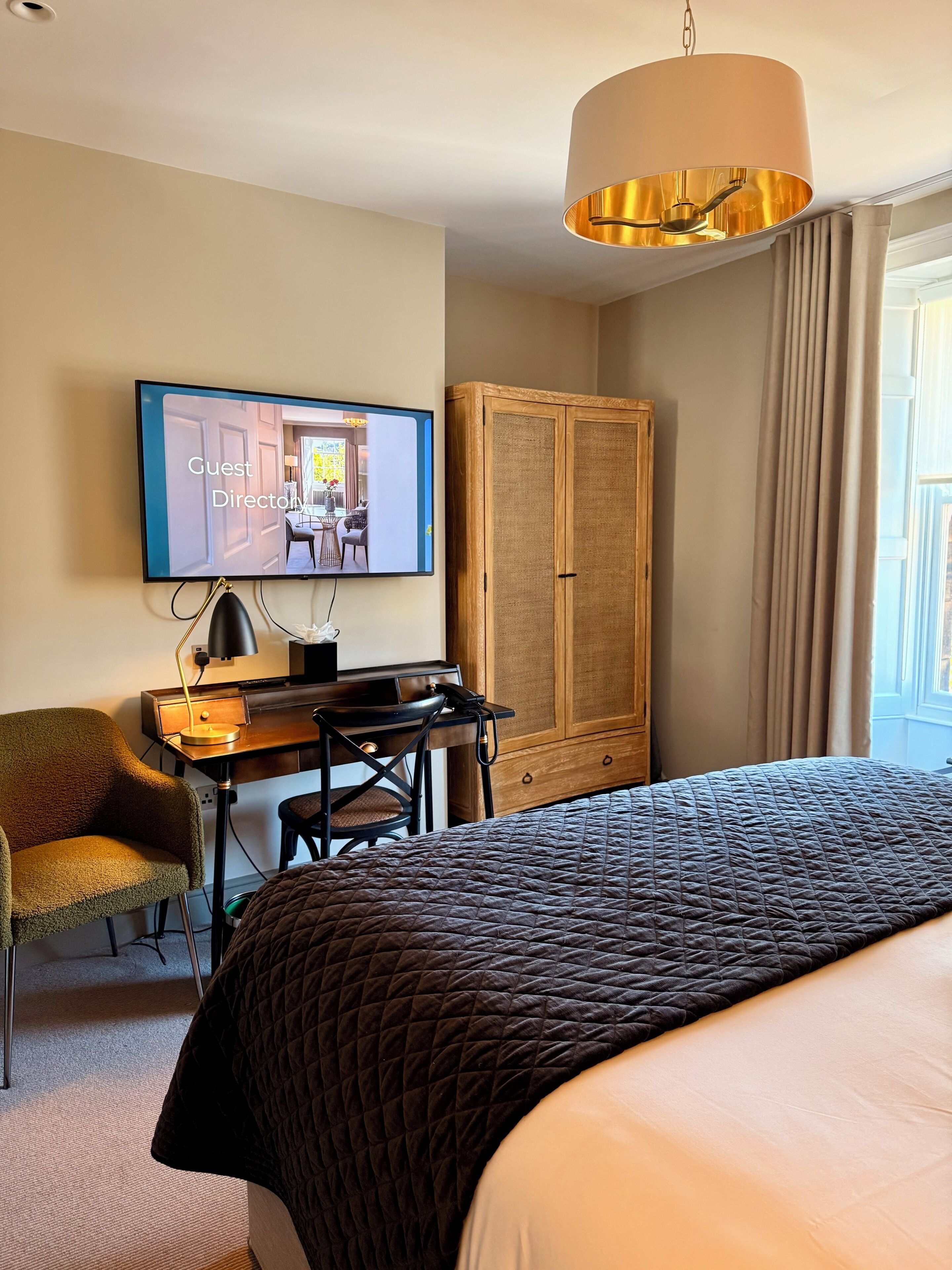 A hotel room with a bed, desk, chair, television, wardrobe, and a window with curtains.