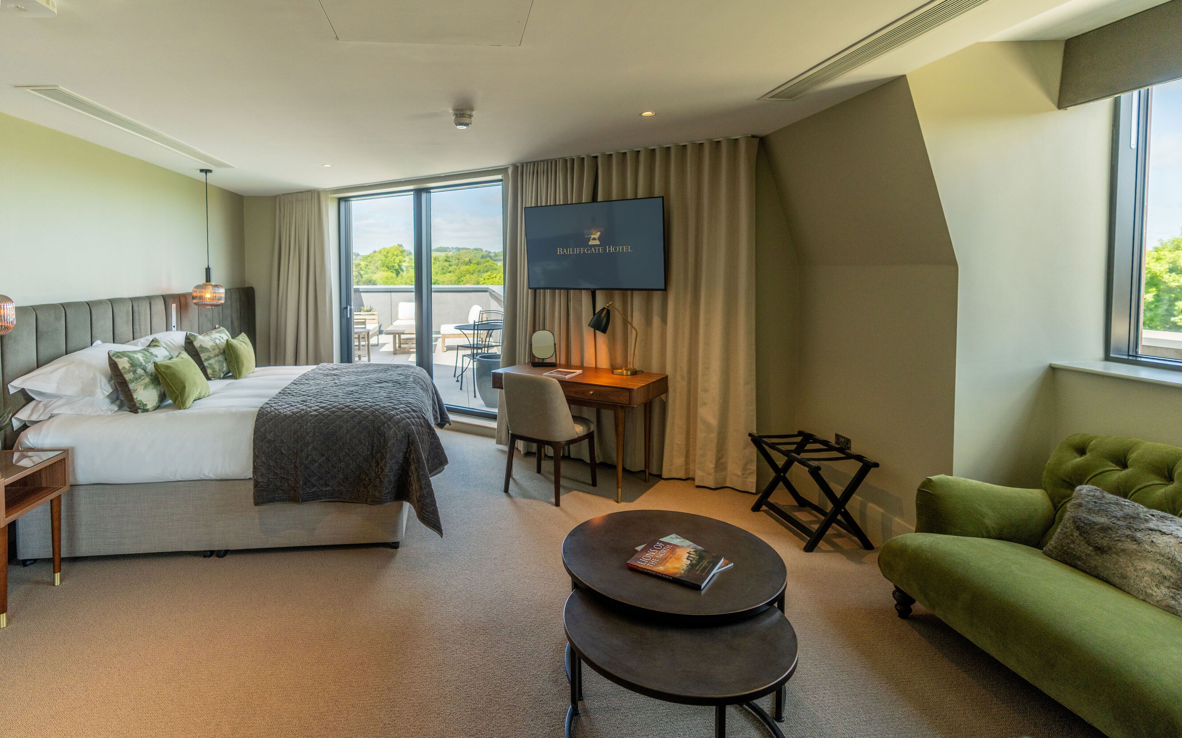 A hotel room with a bed, a desk, a chair, a sofa, a TV, and a balcony with a view.