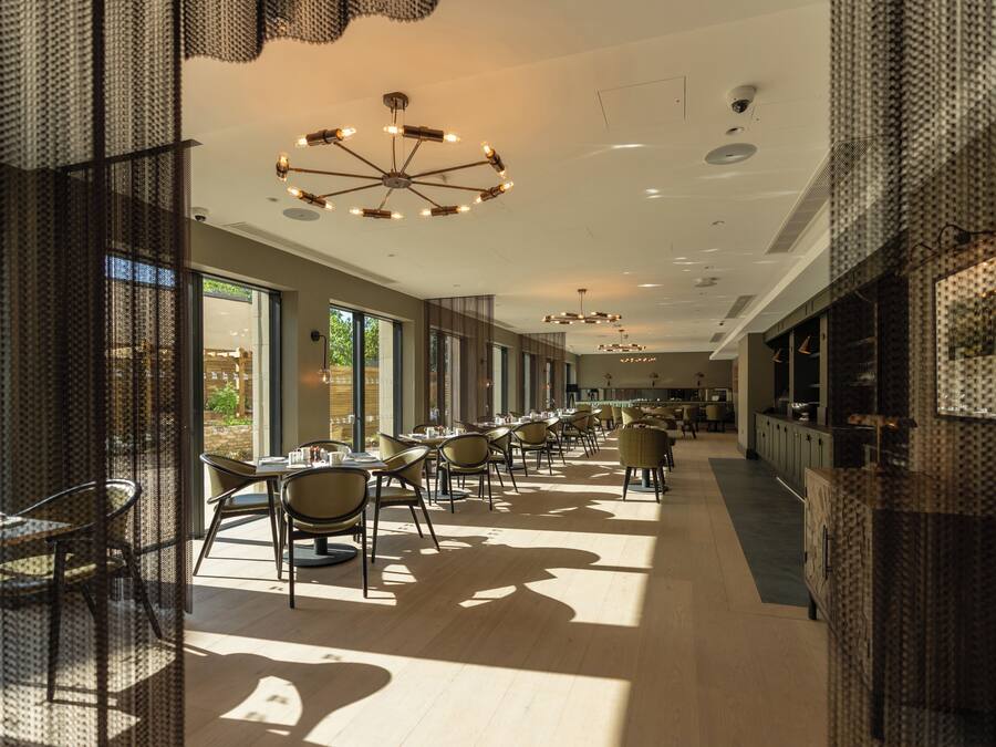 A spacious dining area with multiple tables and chairs, large windows, and modern lighting fixtures.