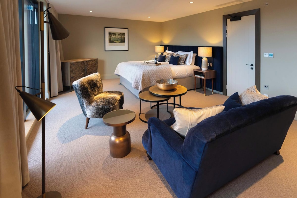 Une chambre d’hôtel avec un lit, un canapé, une chaise, une petite table, une lampe et un tableau au mur.