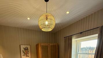 A hotel room with a large bed, a wooden wardrobe, a radiator, a window with curtains, and a ceiling light fixture.
