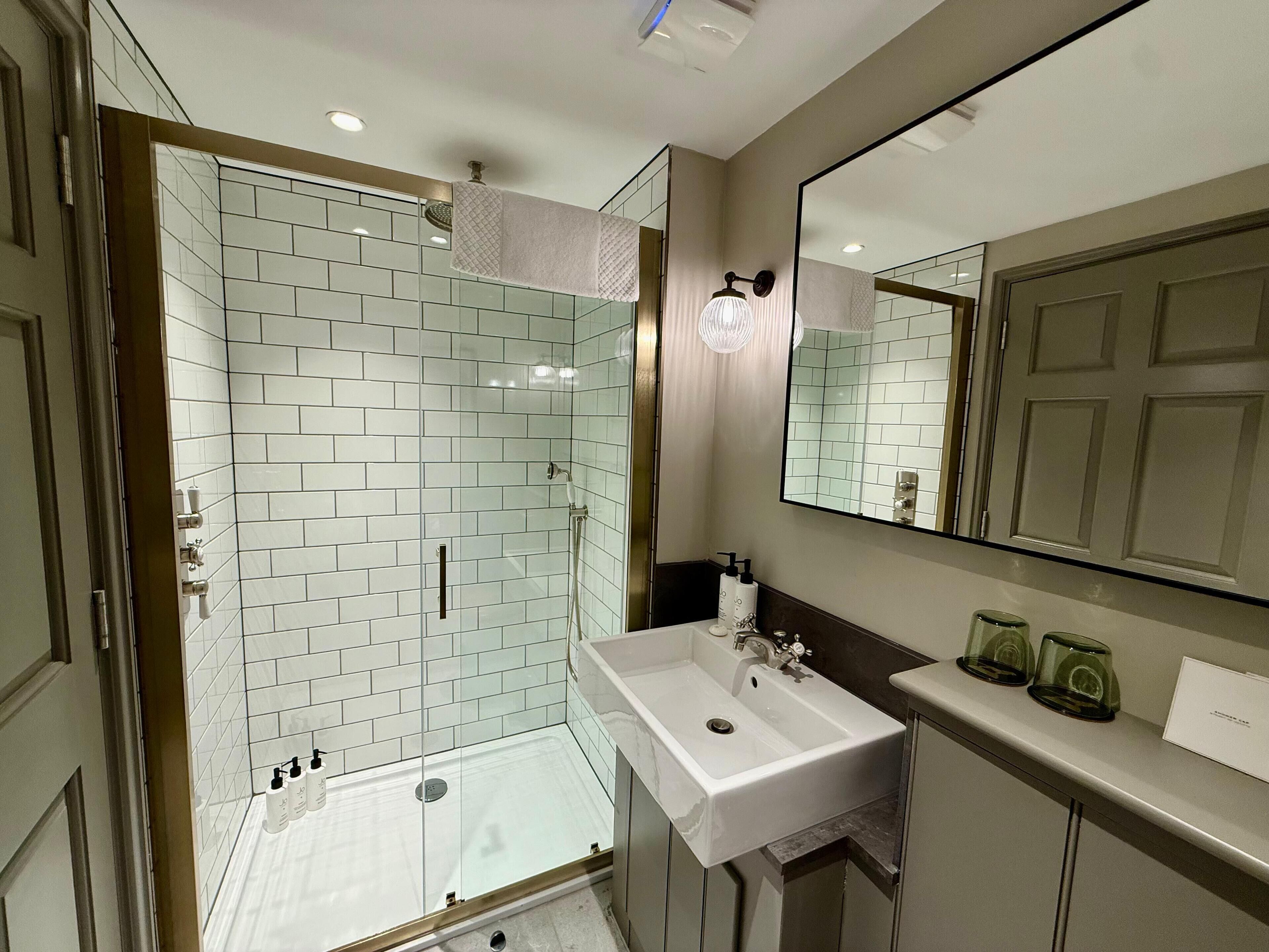 Un baño moderno con ducha envuelta en vidrio, un lavamanos blanco y un espejo grande.