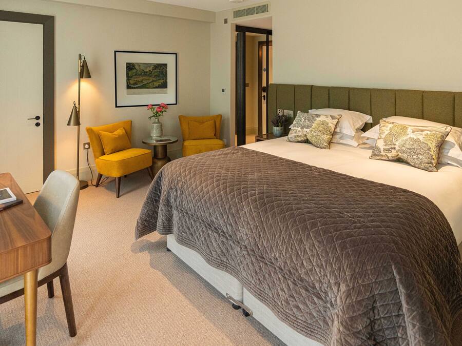 Ein Hotelzimmer mit einem großen Bett, einem Schreibtisch mit Stuhl, einem kleinen Tisch mit Lampe und einem gerahmten Bild an der Wand.