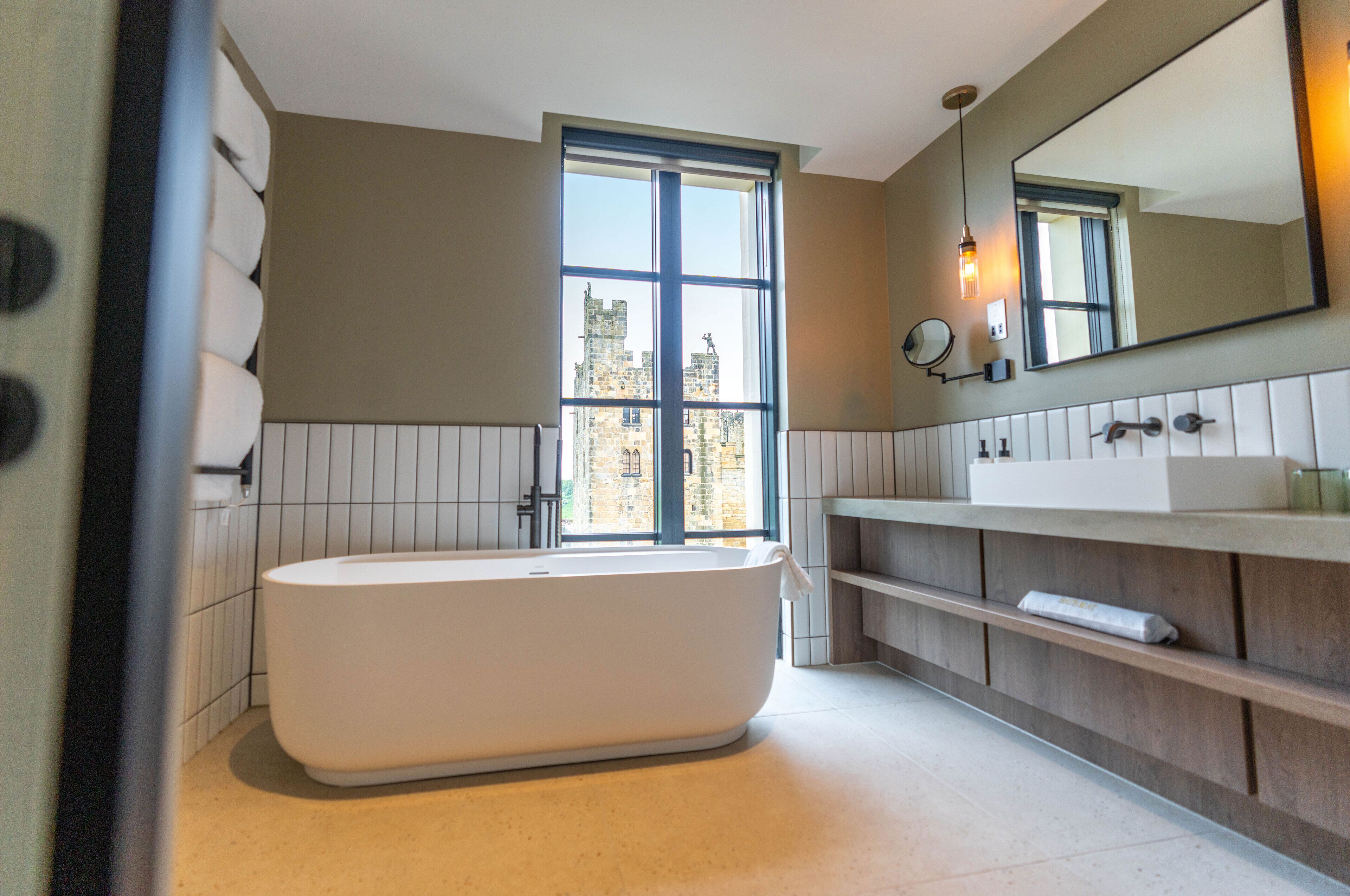 Une salle de bain moderne avec une baignoire sur pieds, un grand miroir et une fenêtre offrant une vue sur le paysage urbain.