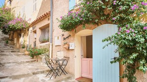 Une ruelle pavée étroite, avec une table et des chaises devant un bâtiment dont la porte est bleue et les volets, roses.