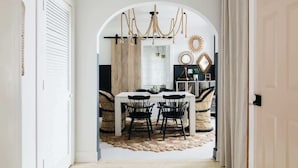 Un coin repas avec une table et des chaises blanches, un lustre et un miroir décoratif.