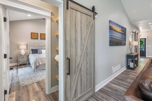 A modern interior with a sliding barn door, a bed with a nightstand, a painting, and a leather bench. - Modern Egg Harbor Home | Dog-Friendly + Fire Pit (Egg Harbor)