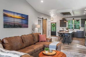 A modern living room with a brown leather sofa, a coffee table, and a large painting of a sunset. - Modern Egg Harbor Home | Dog-Friendly + Fire Pit (Egg Harbor)