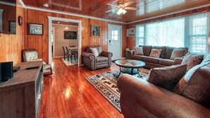 A cozy living room with wooden floors, a ceiling fan, a sofa, a coffee table, and a TV.