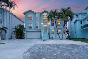 A multi-story residential building with a garage, palm trees, and a driveway.