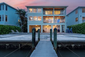 A waterfront property with a dock leading to a multi-level building, featuring balconies and outdoor seating.