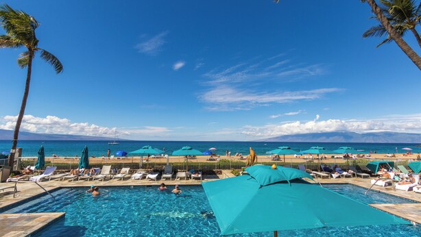 Area piscina con lettini e ombrelloni, cielo sereno e vista sull'oceano.