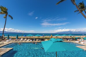 Un espace piscine avec des chaises longues et des parasols, un ciel dégagé et une vue sur l’océan.