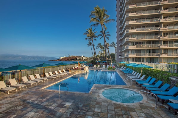 Relax by the oceanfront pool surrounded by lounge chairs and umbrellas, with breathtaking views of the distant mountains.