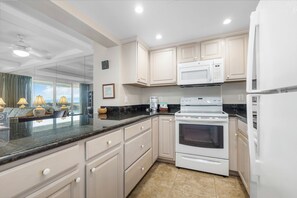 Modern kitchen with a large island, white appliances, and a window offering a view of the outdoors.