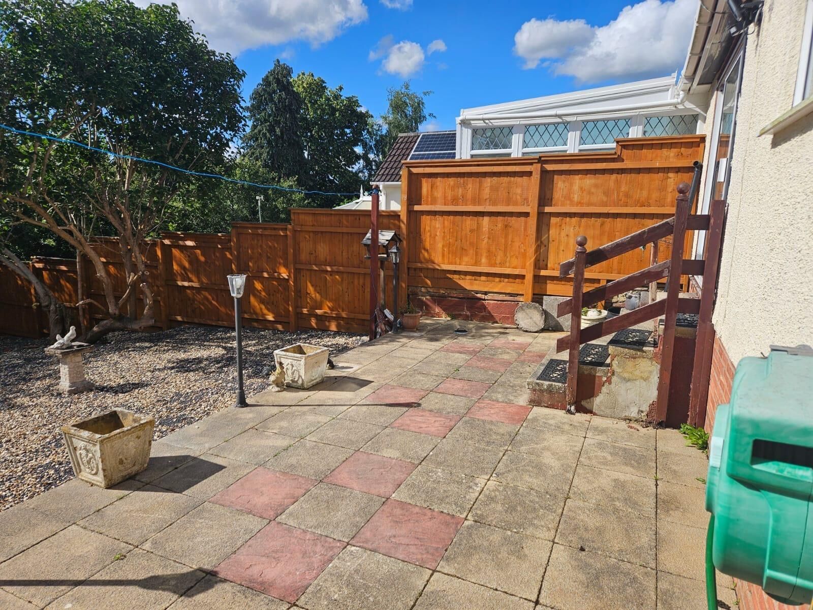 A backyard with a wooden fence, a stone planter, and a green trash bin.