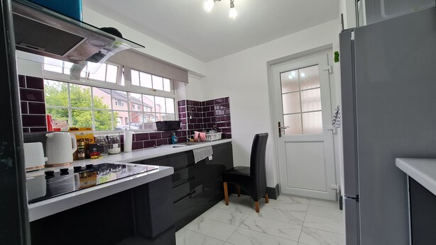 Une cuisine moderne dotée d’un îlot central, de meubles de couleur noire et d’une fenêtre donnant sur des maisons.