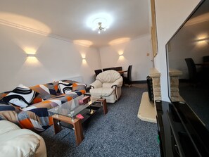 A living room with a sofa, armchair, and coffee table. There is a fireplace with a stone surround and a television on a stand.