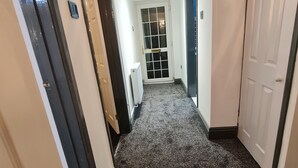 Un couloir étroit, dont le sol est recouvert de moquette, les murs sont peints en blanc et une porte se trouve au fond.