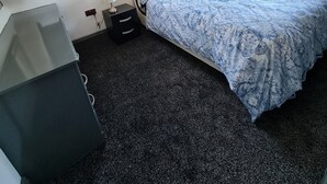 Une chambre à coucher avec un lit, des rideaux, une lampe, un radiateur et une petite armoire.