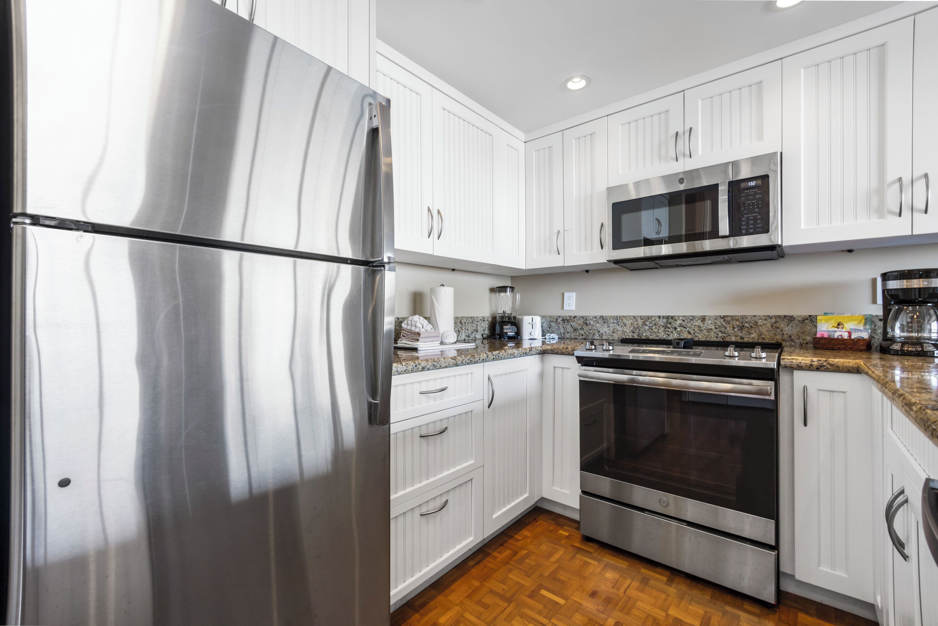A modern kitchen with stainless steel appliances, white cabinetry, and a granite countertop.