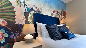 Ein Schlafzimmer mit Bett, Kissen, Nachttisch, Lampe und Wandbild.