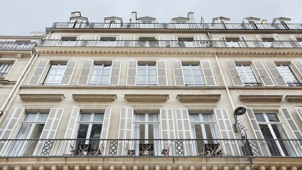 A multi-story building with white shutters, balconies with wrought iron railings, and a uniform architectural style. - Charming apartment Louvre Museum / Concorde (Paris)