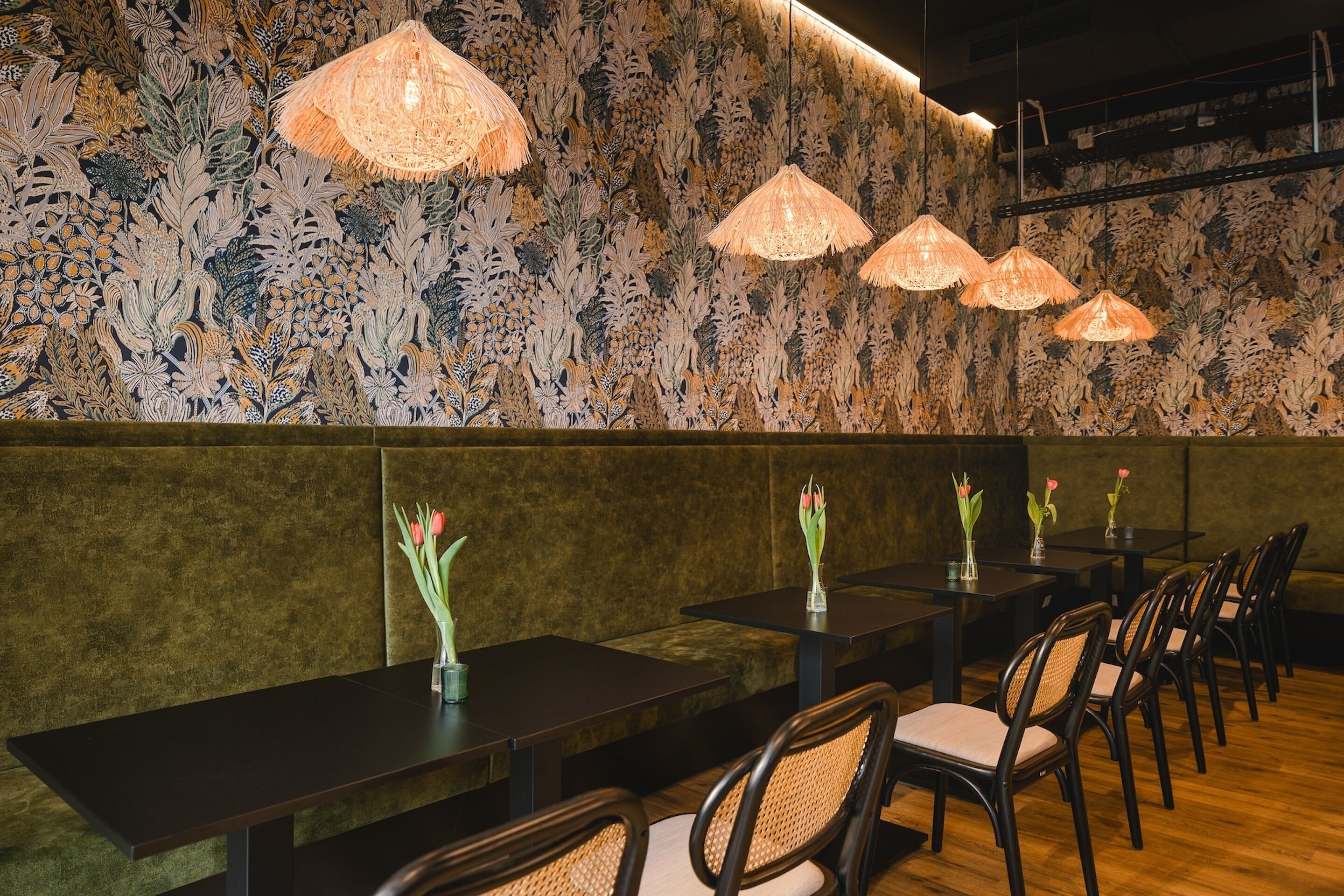 A restaurant with long tables and chairs, floral wallpaper, and hanging lamps.