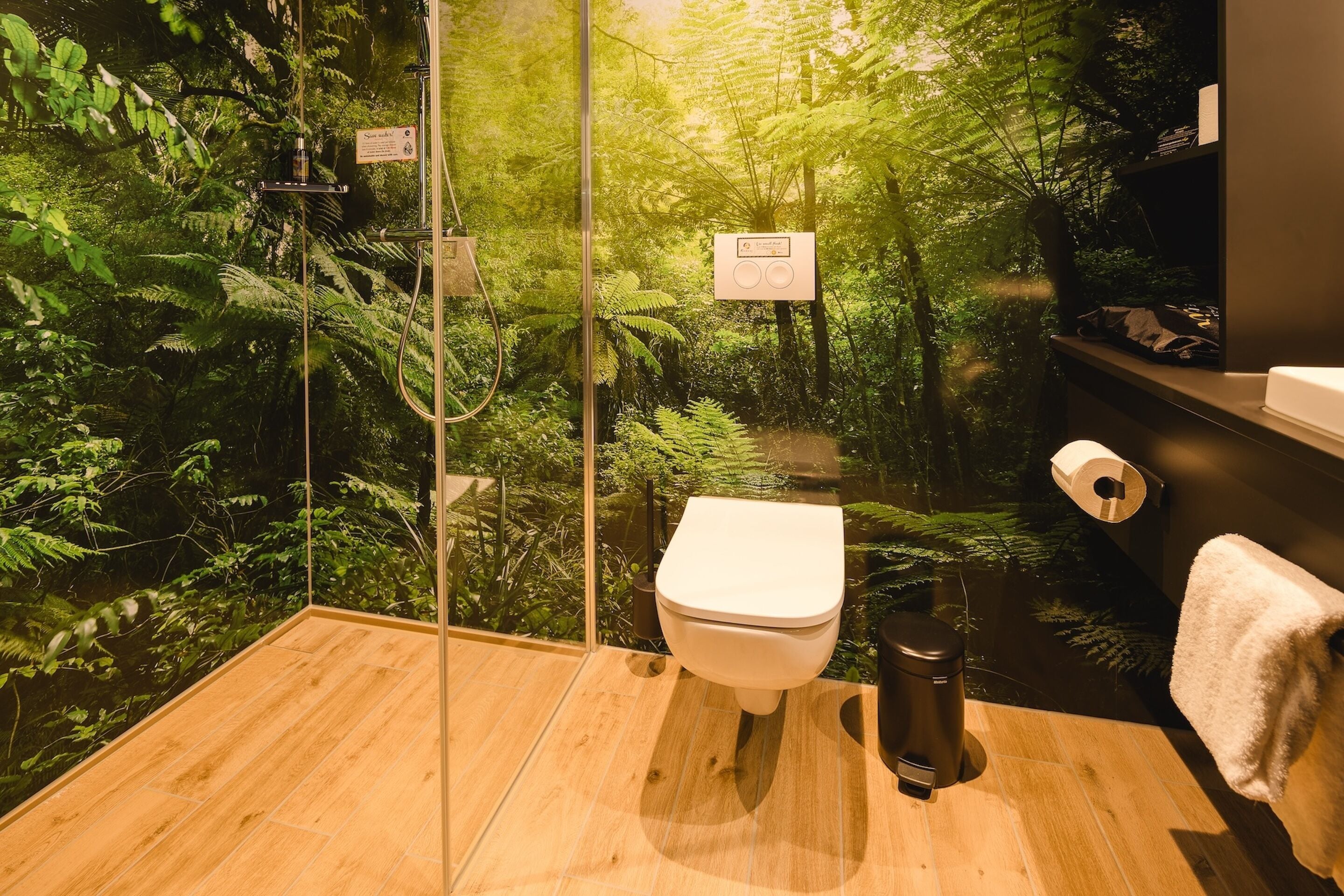 A bathroom with a glass enclosure, a toilet, a trash bin, and a towel rack.