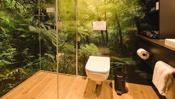Un baño con cabina de vidrio, inodoro, cubo de basura y perchero para toallas.