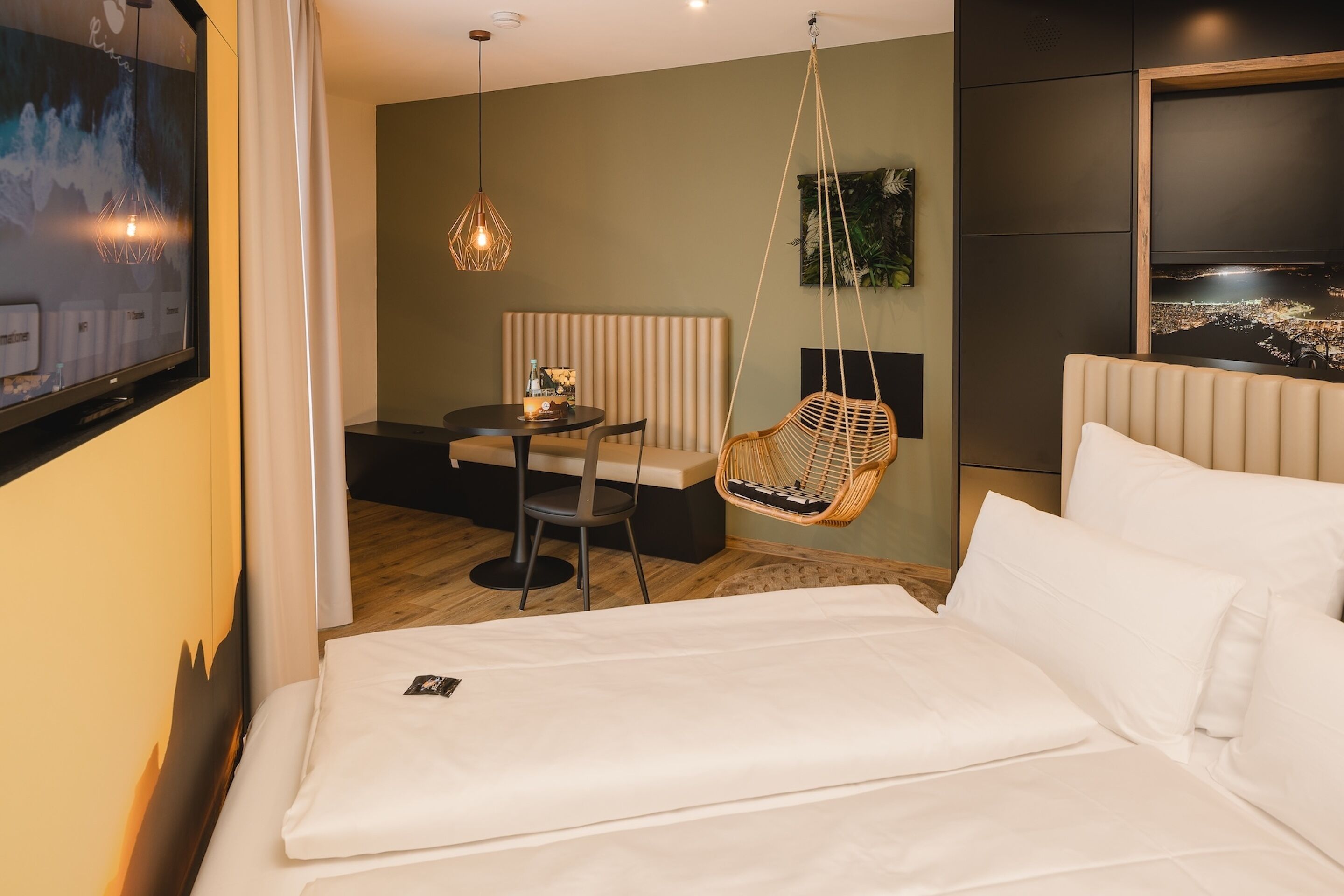 Habitación de hotel con cama, una silla colgante, una mesita con silla, televisor y vista panorámica de la ciudad.
