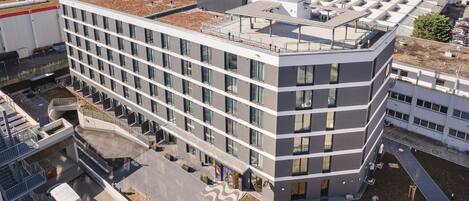 Un edificio moderno de varios pisos con techo plano, ventanas grandes y un estacionamiento al frente.