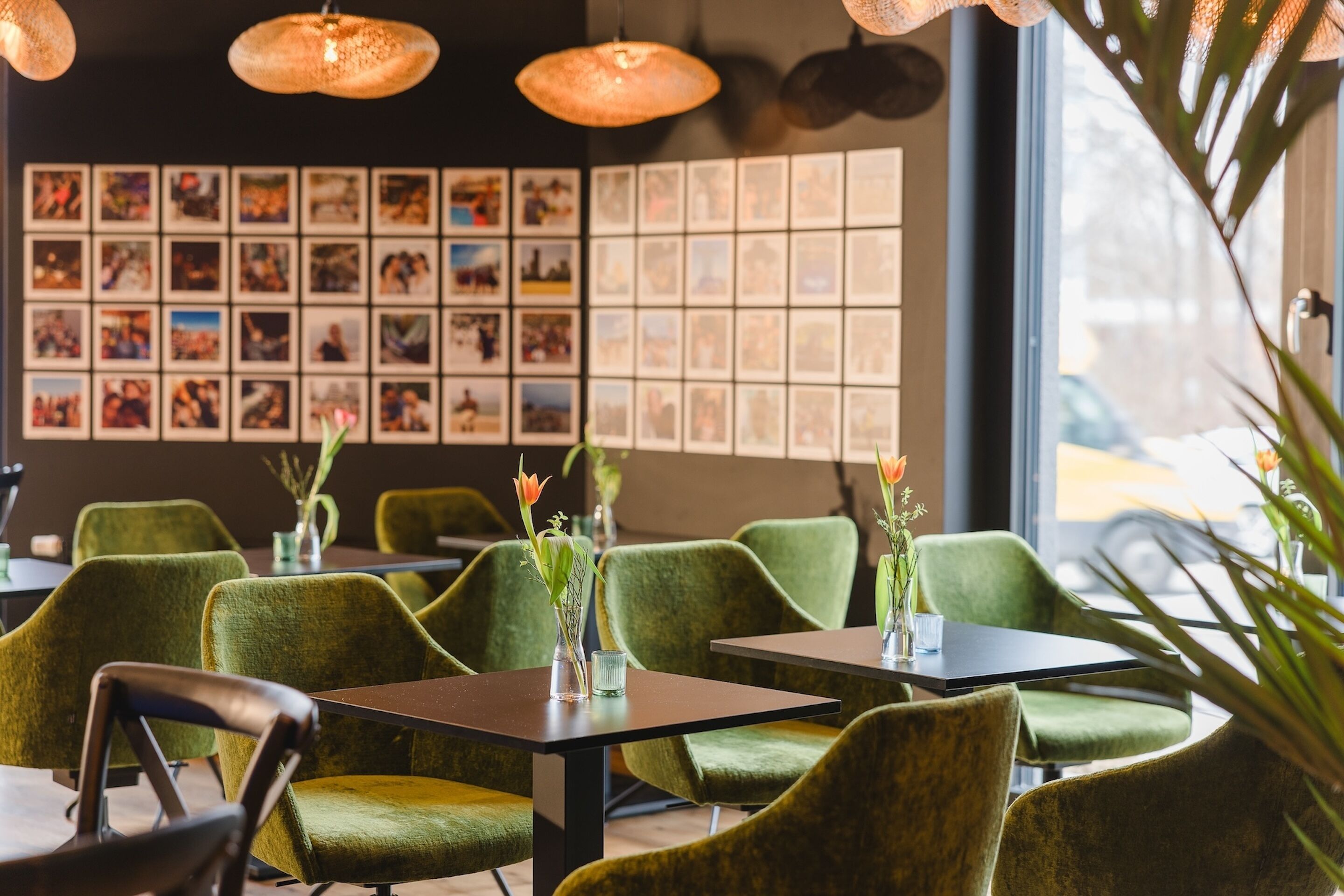 A restaurant interior with green upholstered chairs, tables, and hanging pendant lights.