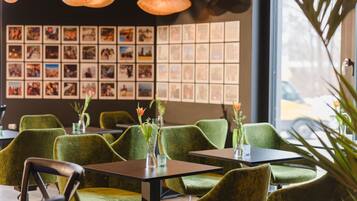 A restaurant interior with green upholstered chairs, tables, and hanging pendant lights.