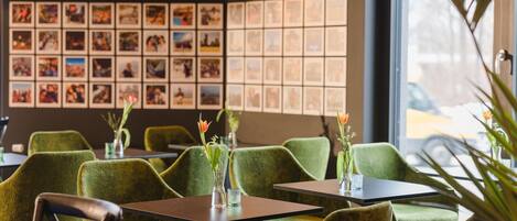 A restaurant interior with green upholstered chairs, tables, and hanging pendant lights.