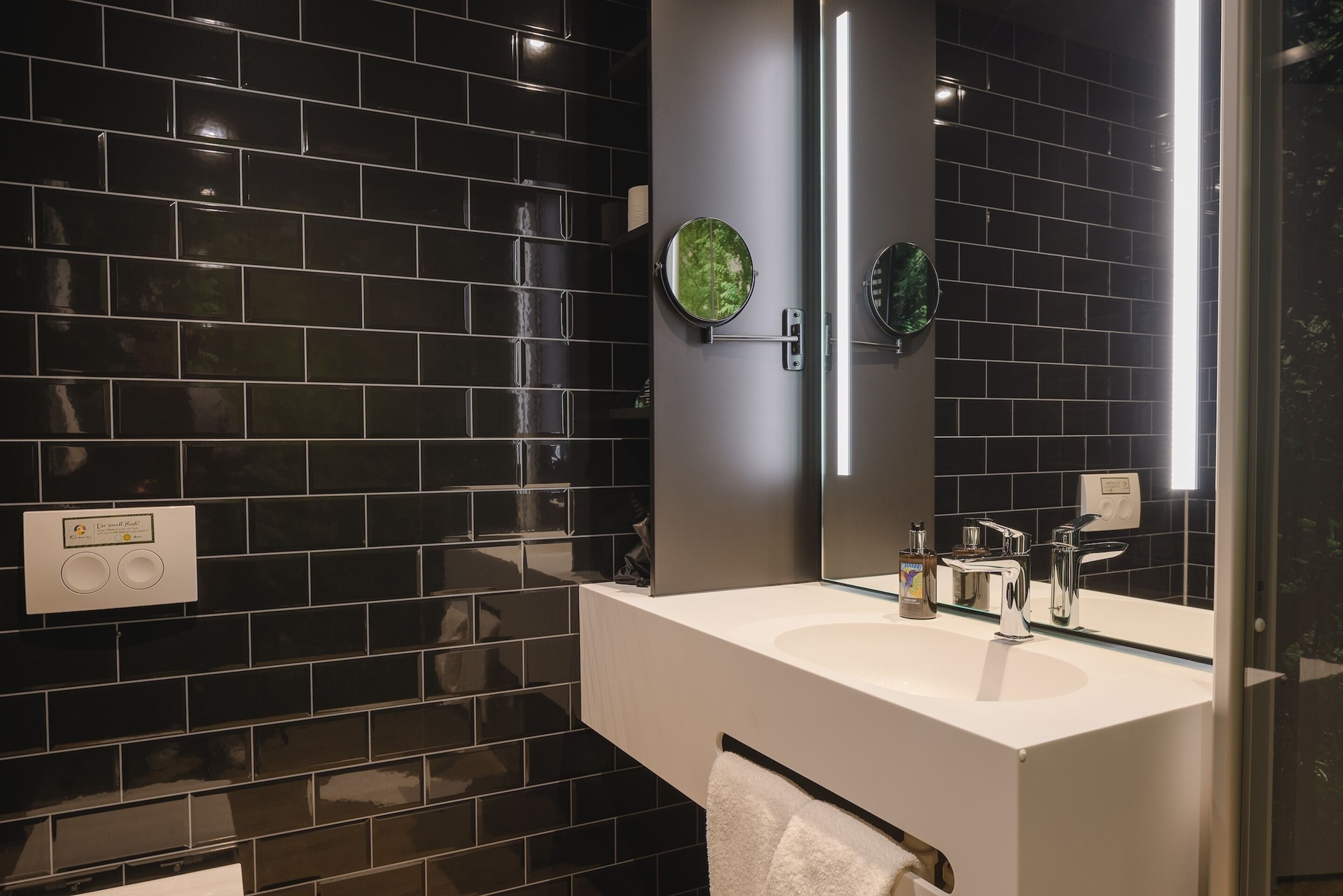 A modern bathroom with black tiled walls, a white sink, and a large mirror.