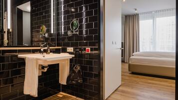 Ein modernes Badezimmer mit schwarzen Fliesenwänden, einem weißen Waschbecken und einem großen Spiegel.