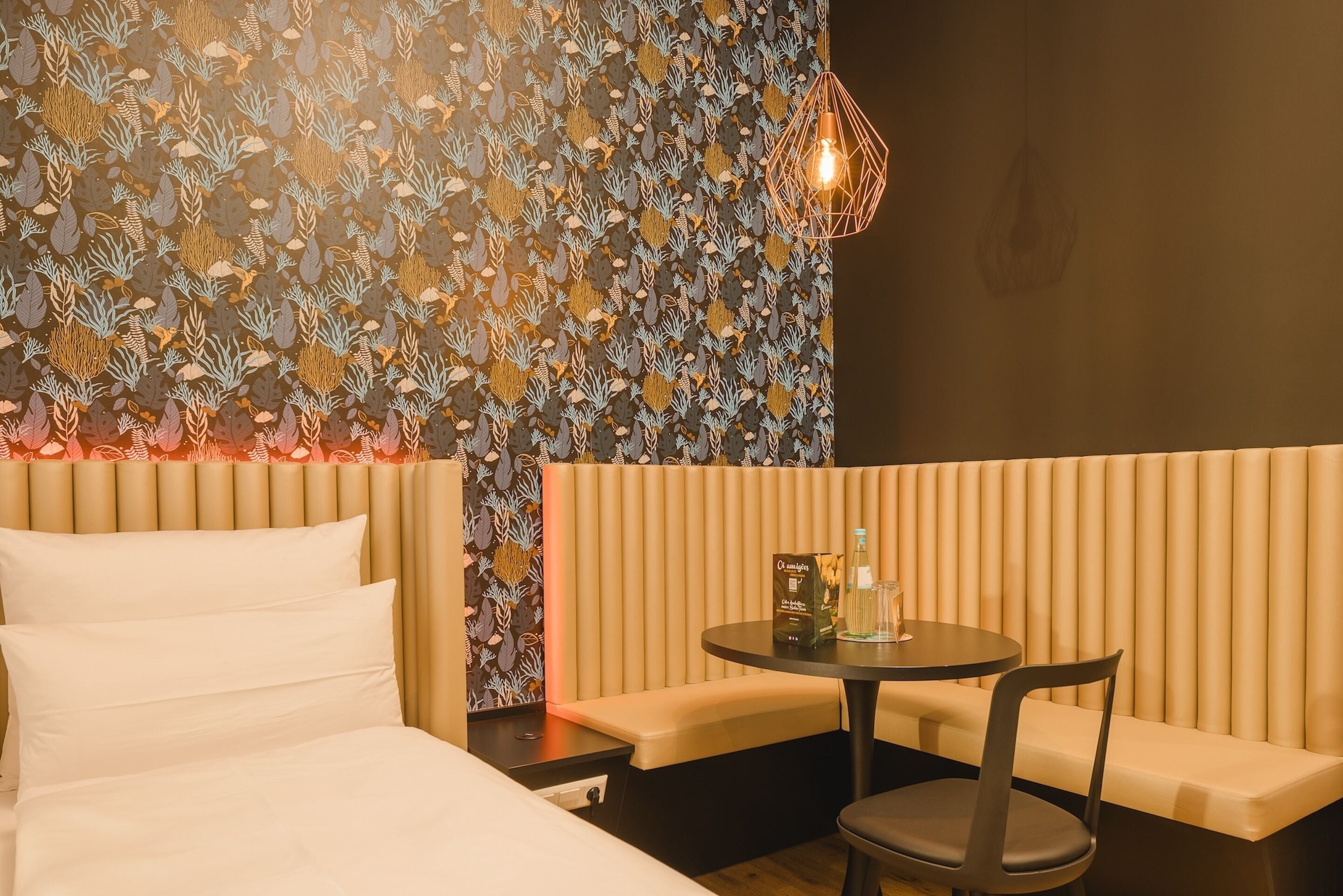 A hotel room with a bed, a seating area with a table and chairs, and a patterned wall.