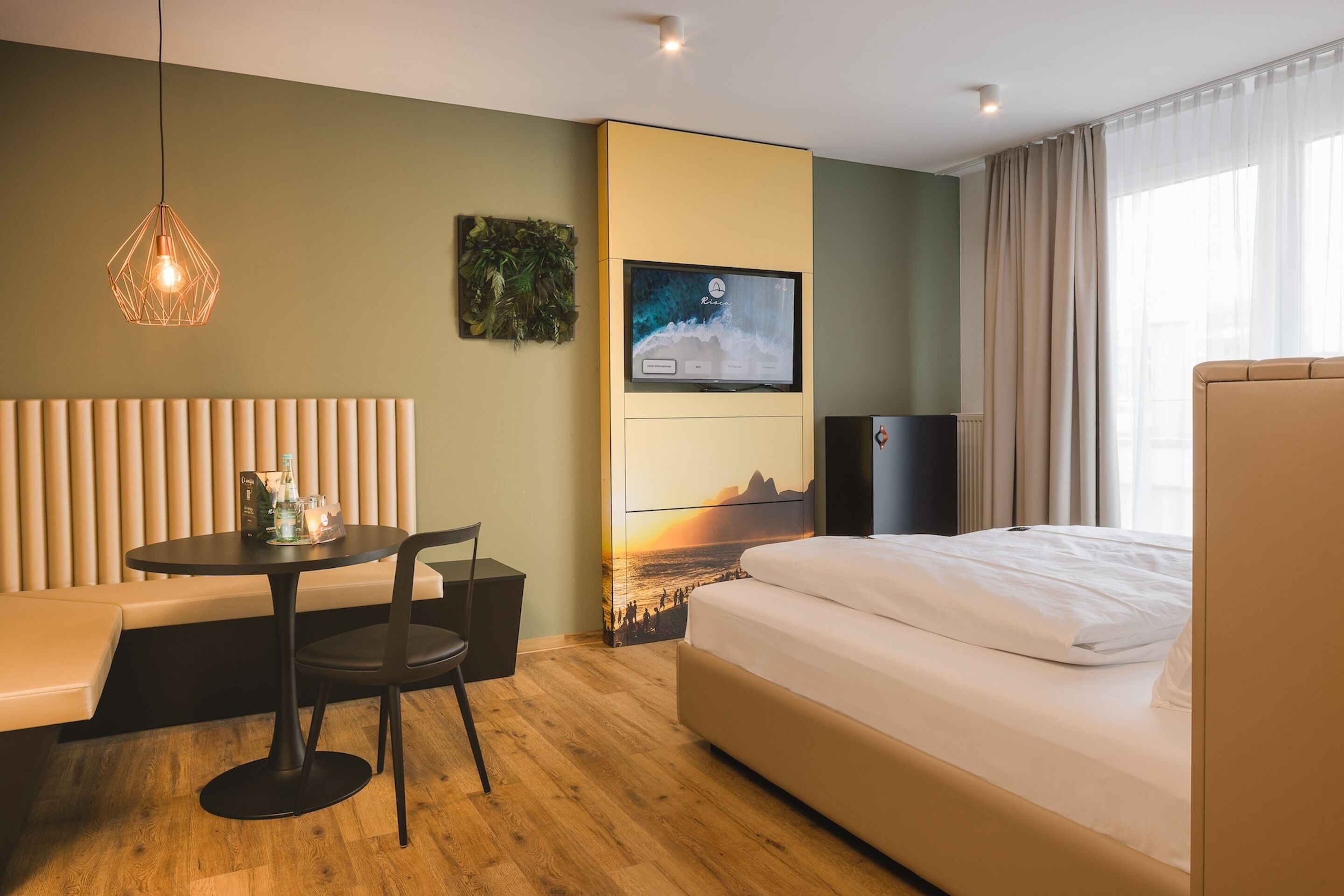 A hotel room with a bed, a seating area with a table and chairs, a television mounted on the wall, and a window with curtains.