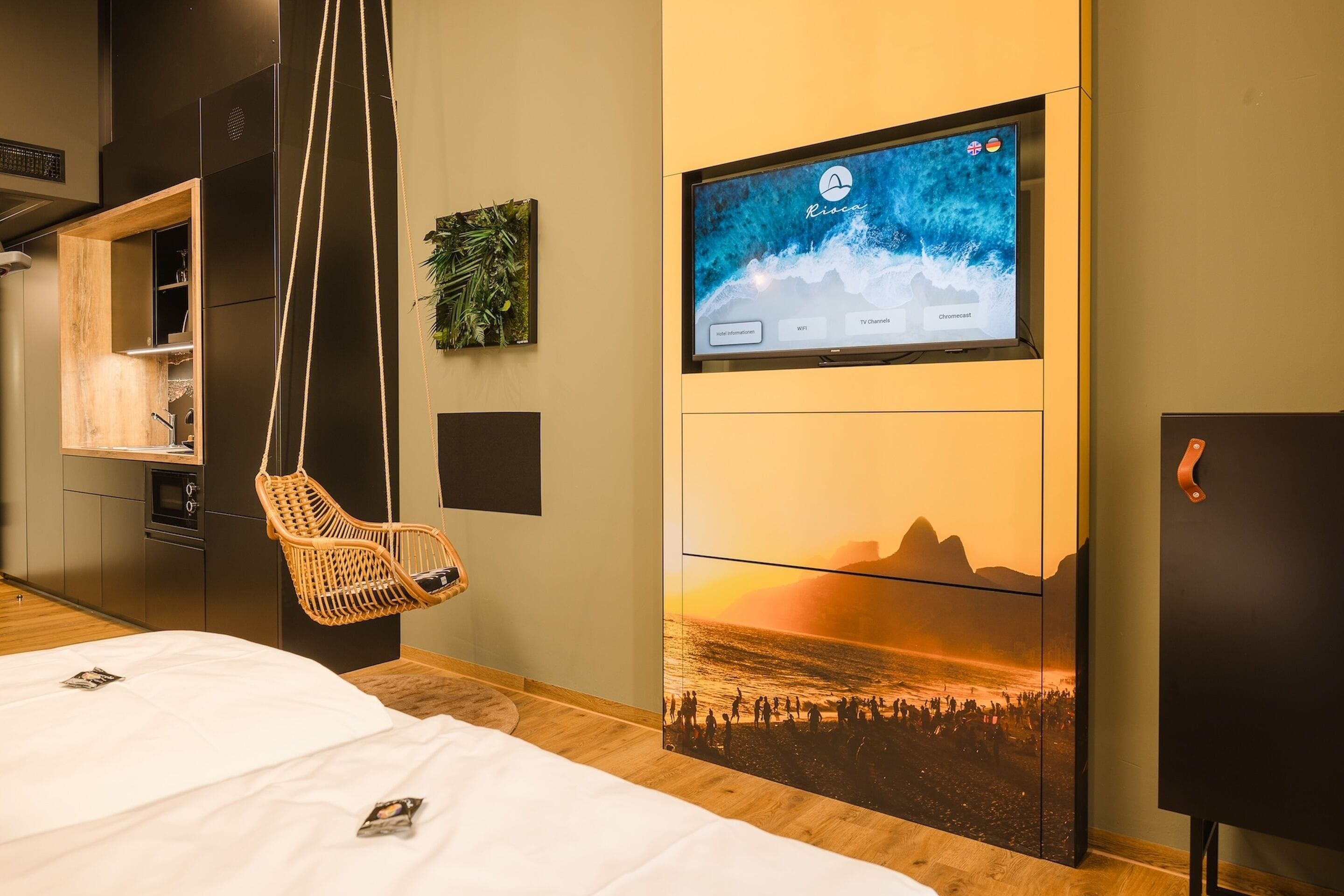 Una habitación de hotel moderna con un televisor de pantalla plana grande montado en la pared, un sillón colgante, una cama con ropa de cama blanca y un mural panorámico.