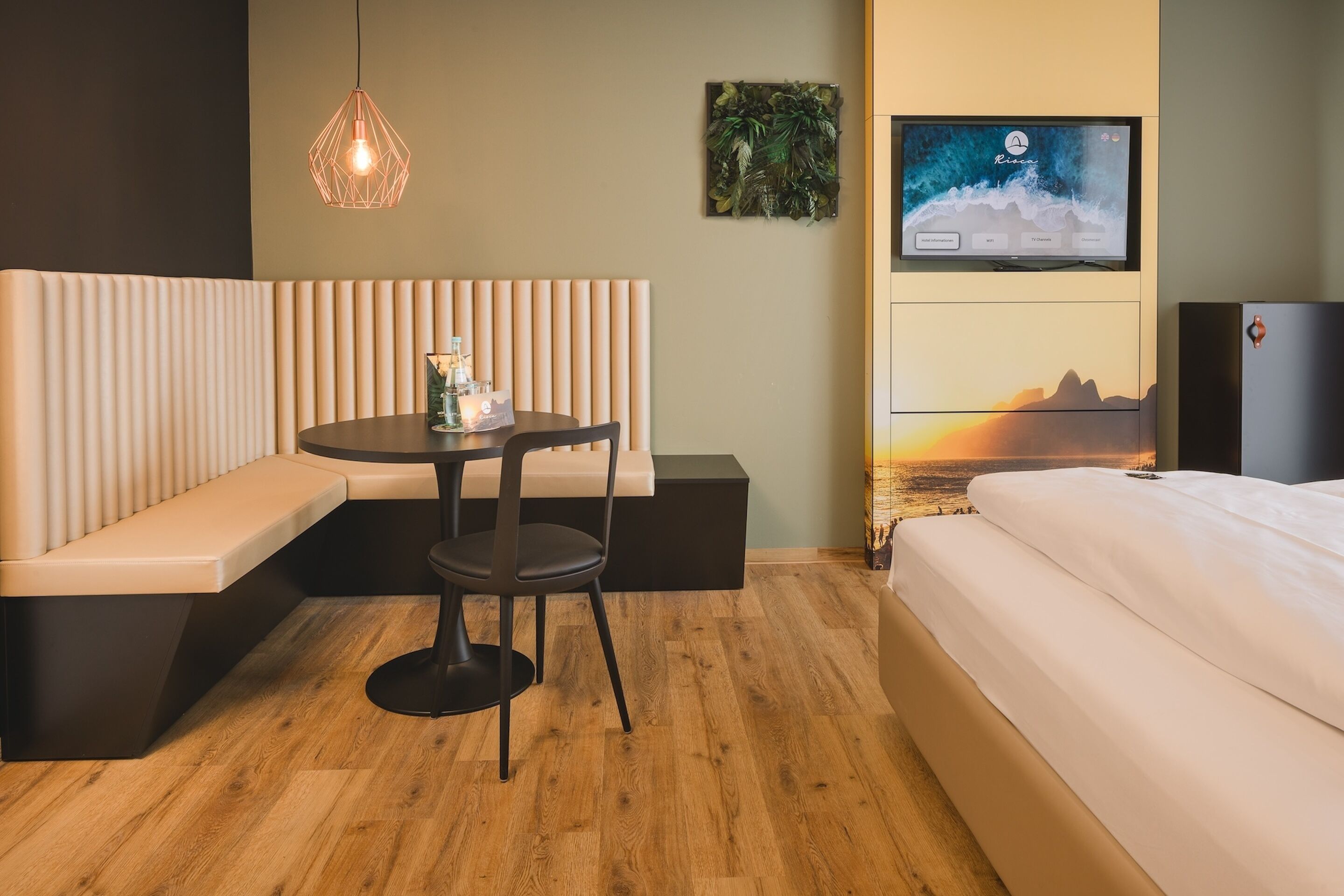 Una habitación de hotel moderna con una cama, un área de descanso con una mesa y sillas, un televisor montado en la pared y suelo de madera.