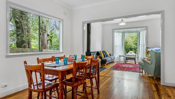 A dining area with a wooden table and chairs, a sofa, and a TV in a living room.