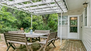 An outdoor patio with a wooden table and benches, a pergola, and a brick floor.