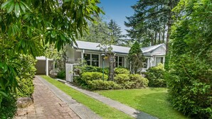 A house with a paved driveway, a well-maintained lawn, and a variety of trees and shrubs.