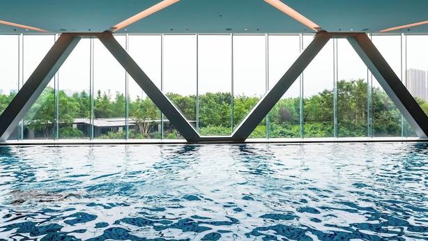 An indoor swimming pool with a geometric ceiling design and large windows offering a view of greenery and buildings. - Sheraton Taizhou (Taizhou)