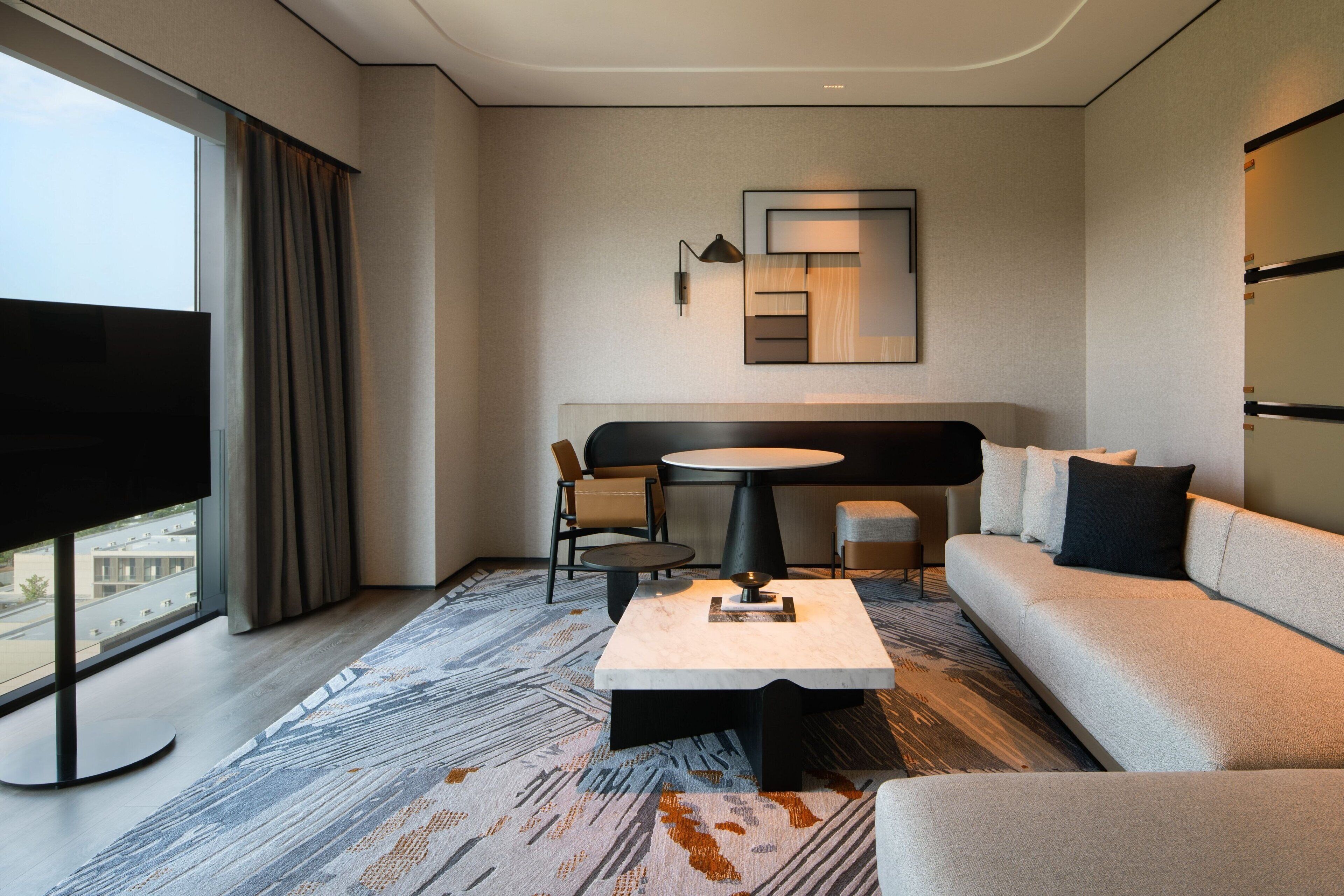 Ett modernt hotellrum med ett stort fönster, en soffa, ett runt bord och en tv.