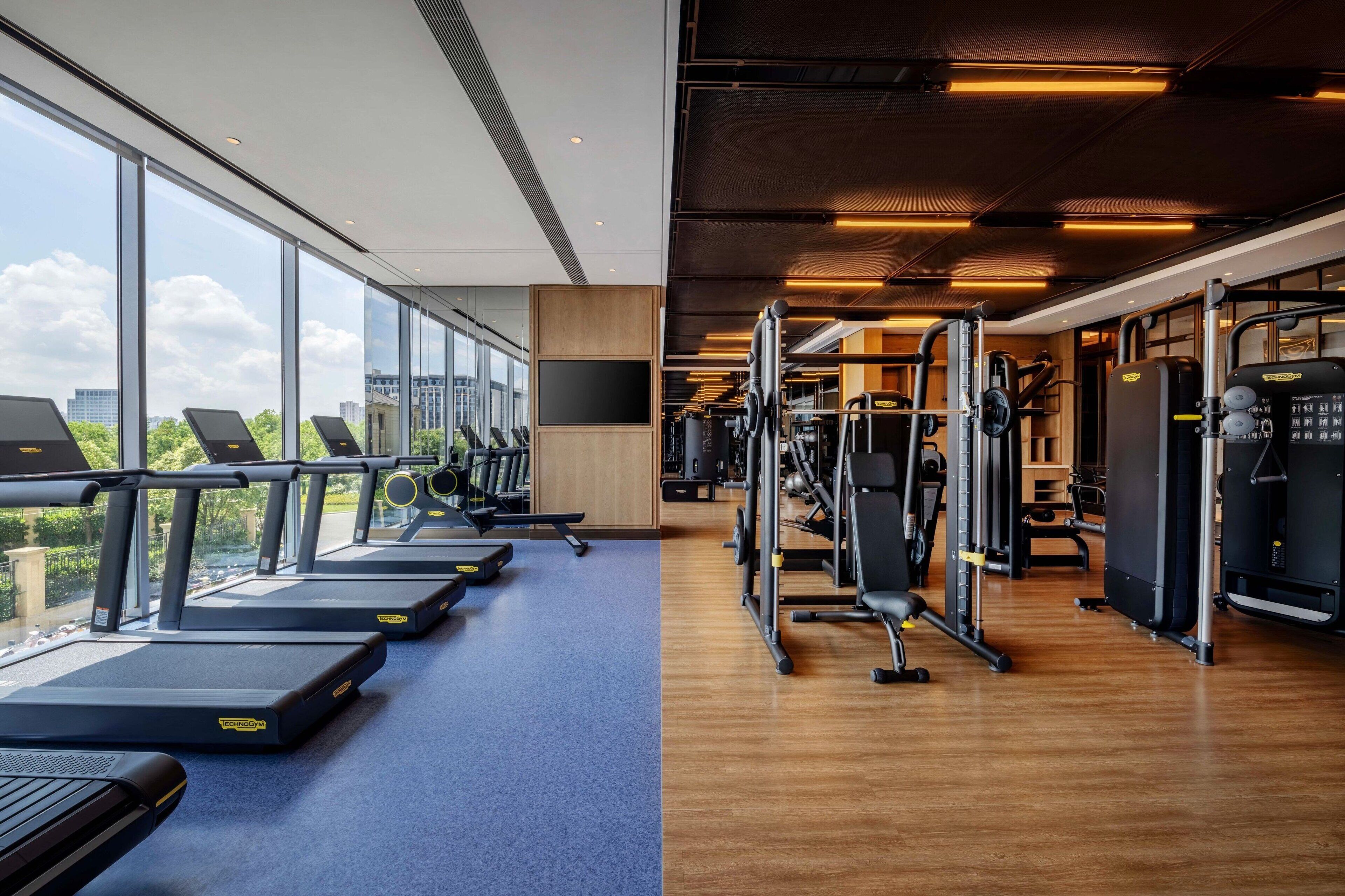 A gym with treadmills, weight machines, and a large window overlooking a cityscape.